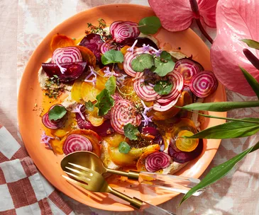 Thin slices of beetroot on an orange plate on top of nut cream and orange juice vinaigrette topped with nasturtium leaves.
