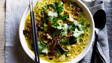 An overhead shot of a bowl brimming with chicken noodle soup, topped with fresh coriander