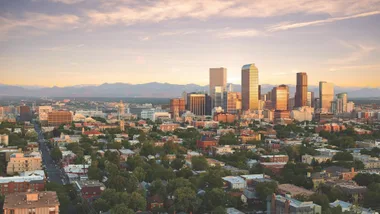 Denver skyline at sunset with the Rocky Mountains in the background.