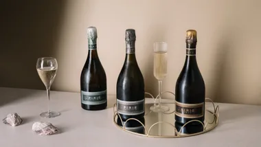 Three Pirie Tasmania sparkling wine bottles on a mirrored tray with two filled glasses and shells.